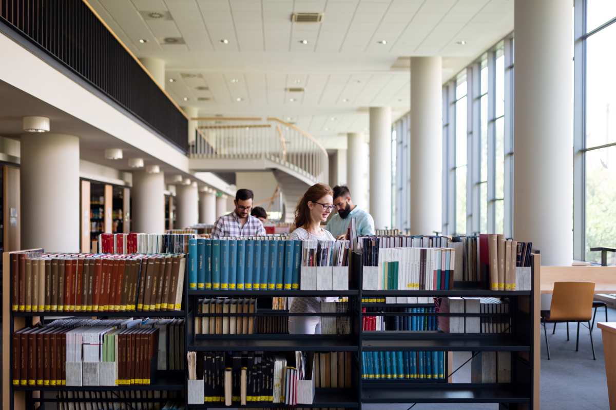 oameni citind carti intr-o biblioteca, carti romanesti sau internationale