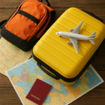 Bagaj de călătorie low-cost – rucsac portocaliu și troler galben așezate pe o hartă a Europei, alături de un pașaport și o machetă de avion.